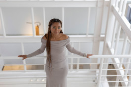 Portrait der Künstlerin Agnes Essonti Luque für die Biennale für Freiburg 3, 2025. Sie steht angelehnt an einem weißen Geländer und schaut nach oben zur Kamera.