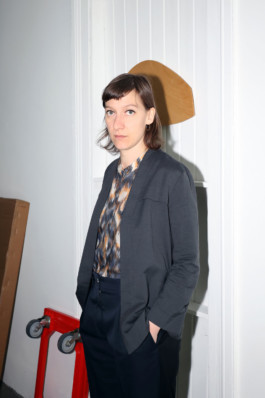 Portrait der Künstlerin Celine Baumann für die Biennale für Freiburg 3, 2025. Sie steht seitlich vor einem Vorhang.