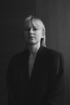 Portrait der Künstlerin Christina Sperling für die Biennale für Freiburg 3, 2025. Das bild ist schwarz-weiß vor einem dunklen Hintergrund und sie trägt einen Blaser.