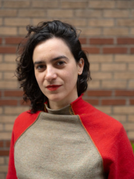 Portrait der Künstlerin Claudia Pagès Rabal für die Biennale für Freiburg 3, 2025. Sie trägt ein rot beiges Oberteil und steht vor einer Steinmauer.