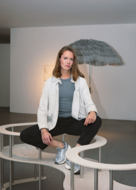 Portrait der Künstlerin Lena Marie Emrich für die Biennale für Freiburg 3, 2025. Sie sitzt auf einer Bank-Installation im Ausstellungsraum.